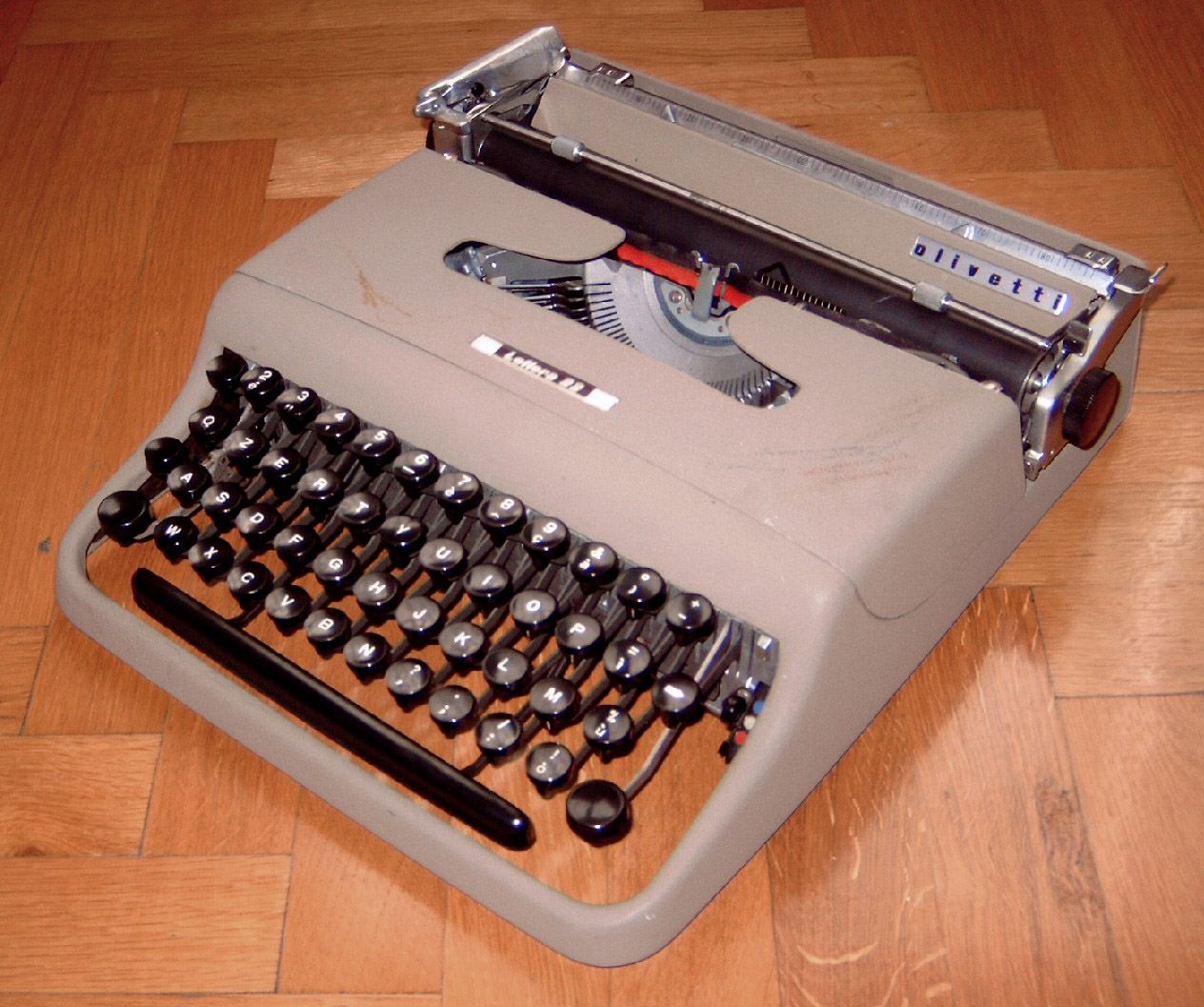 Máquina de escribir portátil Olivetti Lettera 22 de color gris sobre un suelo de parqué