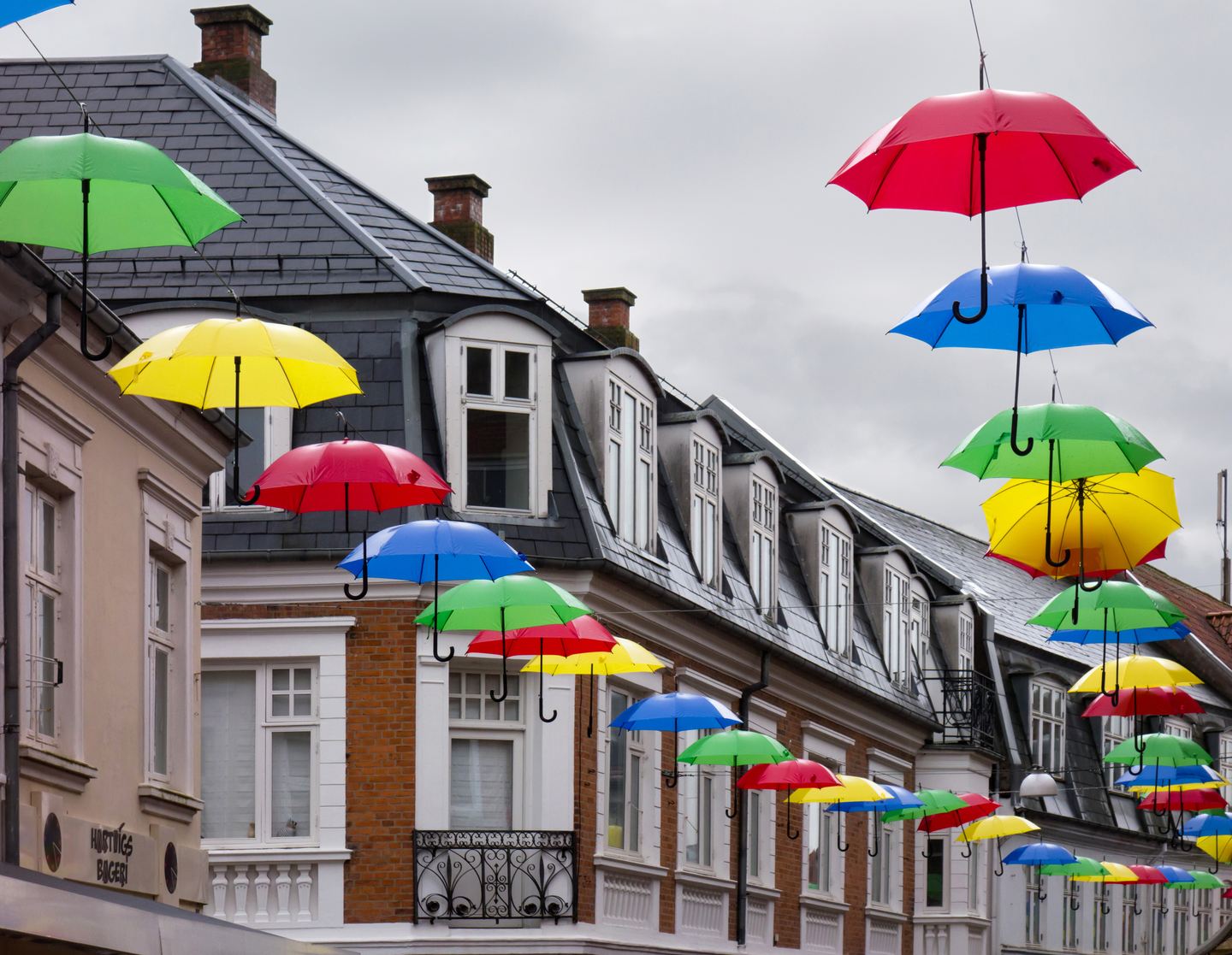 Paraguas de colores colgados sobre una calle comercial con casas de tejado de pizarra