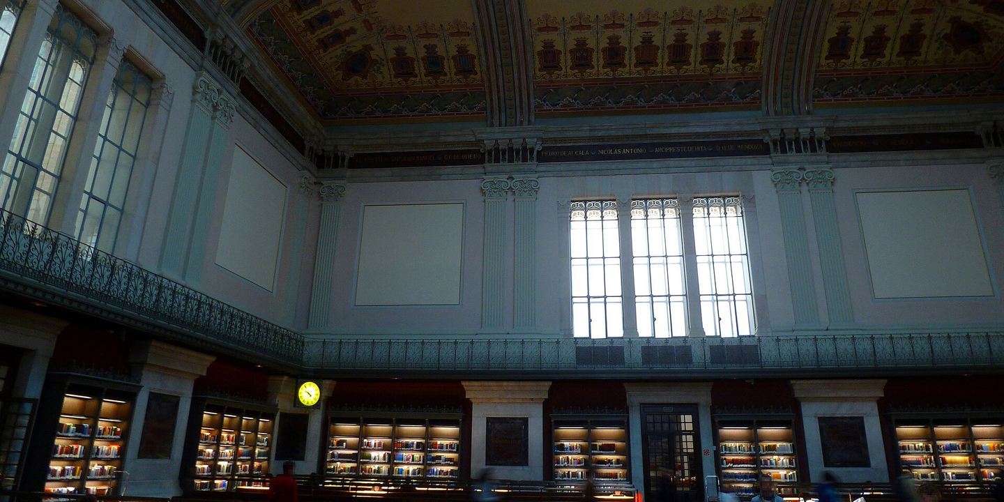 Salón de lectura de la Biblioteca Nacional de España, con techo pintado, lucernario y estanterías iluminadas en la planta baja
